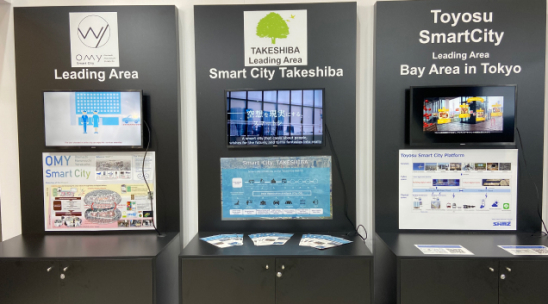 写真:東京都ブース内の様子。先行実施エリアである大手町・丸の内・有楽町エリア、竹芝エリア、豊洲エリアについてのポスターが設置され、サイネージでそれぞれの紹介映像を放映。竹芝エリアと豊洲エリアについてチラシも設置されている。